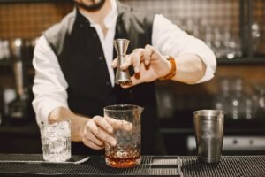 What does bar stand for at the pub? Bartender preparing a cocktail using a jigger and mixing glass at an elegant bar counter.